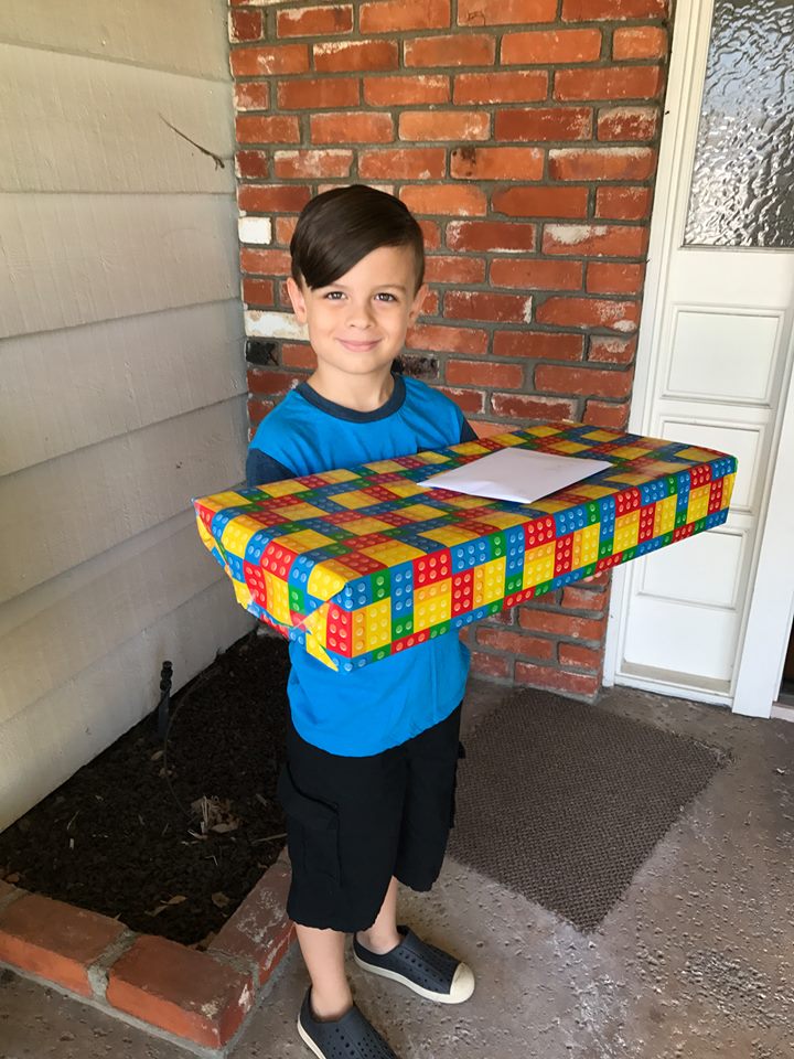 Photo of a child, boy, standing in front of a home folding a present